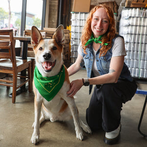 Happy pup wearing a green NPBC bandana. Someone wearing bandana kneeling beside dog.