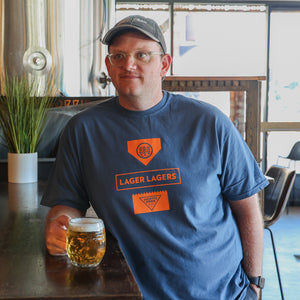 A person wearing a MIdnight Blue tshirt with orange NPBC and Schilling logos, middle text design reads "Lager Lagers"