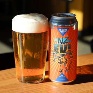 Pint of NZ-Fu! next to a can of North Park Brewing Co. beer on a wooden surface.