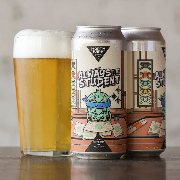 Two aluminum cans of North Park Beer Co 'Always The Student' are shown beside a glass of golden beer with white foam on a tabletop against a soft neutral background.