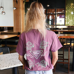 Someone displaying the back of a purpley-pink Disciples of Fu tshirt standing in a casual setting with drinks in the foreground.