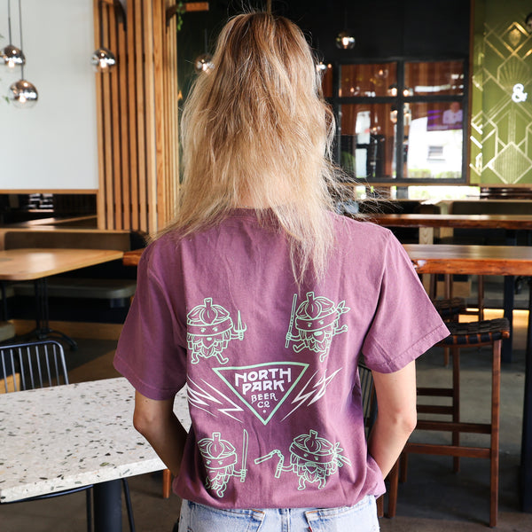 Someone displaying the back of a purpley-pink Disciples of Fu tshirt standing in a casual setting with drinks in the foreground.