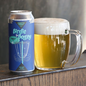 Can of North Park Beer Co 'Birdie to Bogey' beer next to a glass of beer on a wooden surface.