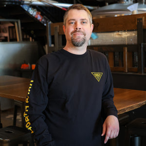 Someone wearing a Black Long Sleeve Tshirt featuring our North Park traingle logo on the front and 'North Park' printed on the right sleeve.