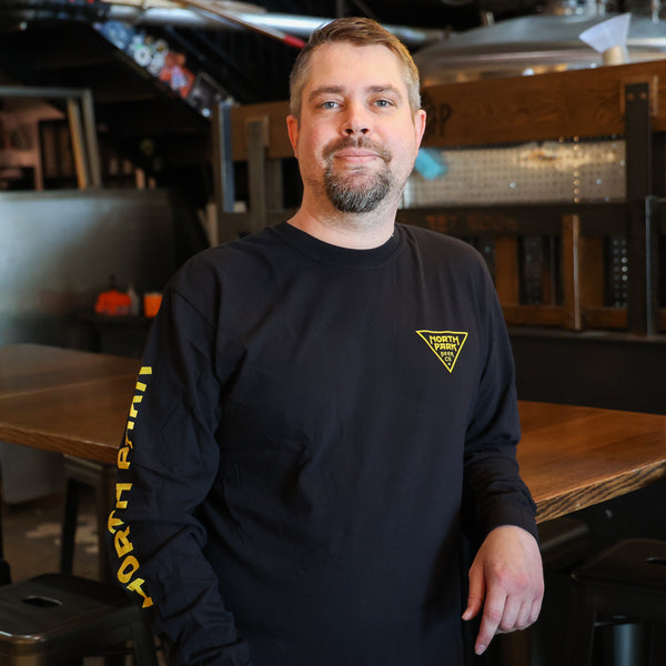 Someone wearing a Black Long Sleeve Tshirt featuring our North Park traingle logo on the front and 'North Park' printed on the right sleeve.