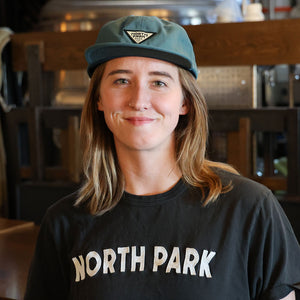 Person wearing a teal triangle logo patch hat and 'North Park' t-shirt in an indoor setting