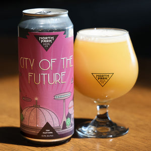 Can of 'City of the Future' beer from North Park Brewing Co. next to a glass of beer on a wooden surface.