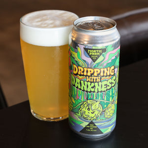 A can of North Park Brewing Co. 'Dripping With Darkness' beside a pint glass filled with golden beer and white foam, set on a dark table.