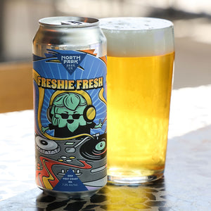 A can of North Park Beer Co Freshie Fresh beer stands next to a glass filled with golden beer and white foam on a patterned tabletop.