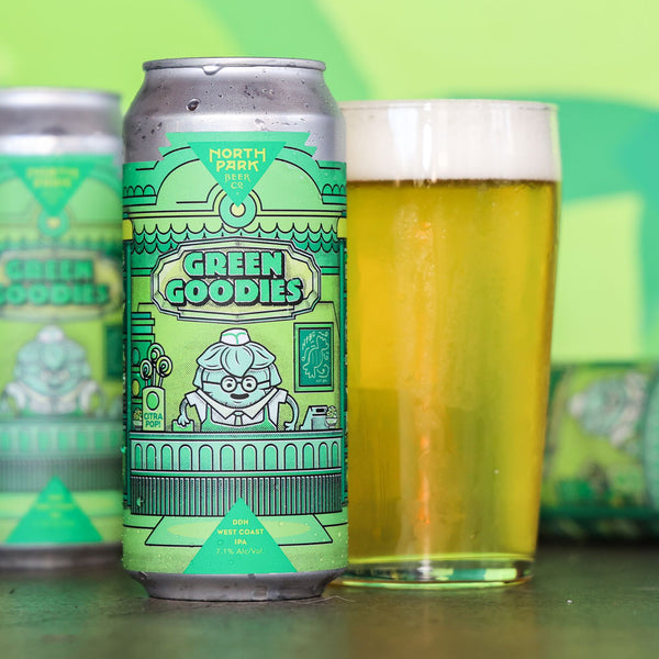 A can of North Park Brewing Green Goodies IPA stands in front of a glass filled with golden beer and foam, on a green background with blurred cans behind.