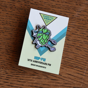 A Hop-Fu! North Park Beer Co. enamel pin on its original backing card, placed on a wooden table.