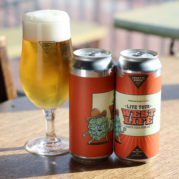 Two cans of Live Your West Life DDH West Coast IPA next to glass of beer