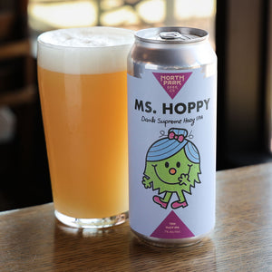 Can of 'Ms. Hoppy' beer next to a glass of beer on a wooden surface