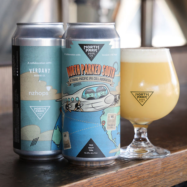 Two cans of North Parked South and a glass of beer on a wooden surface.