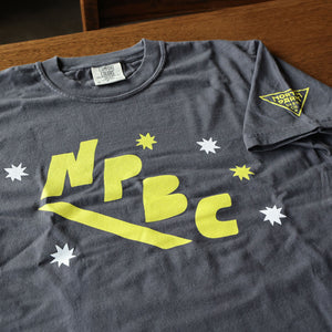 Charcoal Gray t-shirt with yellow 'NPBC' logo on a wooden surface