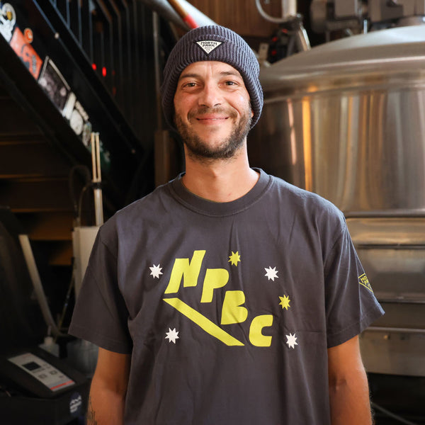 Someone wearing a charcoal gray t-shirt with yellow text and a beanie, standing in a brewery setting.