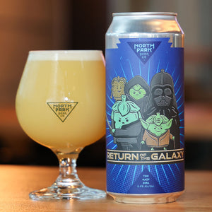 North Park beer can Return of the Galaxy next to a glass of beer on a wooden surface.