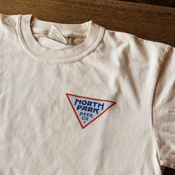 NPBC triangle logo in navy, light blue and orange on the front pocket area of tshirt laying on a table.