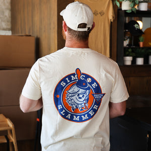 Someone wearing  a beige T-shirt with our Simcoe Slammer logo on the back in navy, light blue and orange.