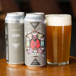 Two cans of 'SIXES' beer with a glass of beer on a wooden surface.