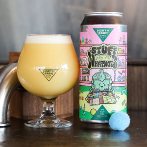 A can of North Park Beer Co. 'Stuff and the Whatnots' next to a tulip glass filled with the golden beer, set on a dark wooden bar counter with a faucet in the background.