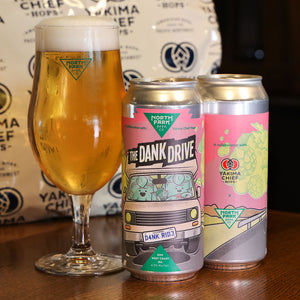 Two cans of 'The Dank Drive' beer with a glass of beer on a wooden surface, by North Park Beer Co.