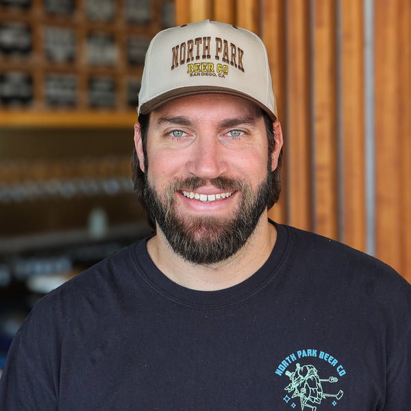 Someone wearing a Beige and Brown Two Tone hat with North Park Beer Co in a collegiate font in brown and yellow embroidery sewn onto the front.