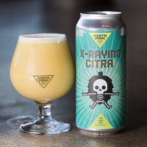 Can of North Park Beer X-Raying Citra next to a glass of beer on a dark background
